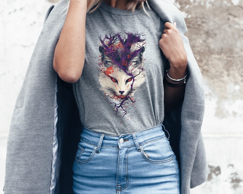 May include: A gray t-shirt with a graphic print of a white fox with purple and orange accents. The fox is surrounded by a stylized tree with purple branches. The t-shirt is being worn by a person.