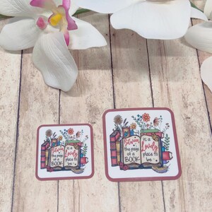 May include: Two square coasters with rounded corners. Each coaster features a design with books, flowers, and the text "Between the page of a book is a lovely place to be" in a whimsical font. The coasters have a maroon border.
