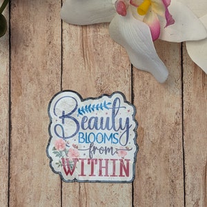 May include: A white sticker with a floral design and the text "Beauty Blooms from Within" in blue and red lettering.