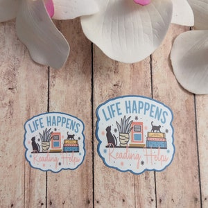 May include: Two blue and white stickers with the text "Life Happens Reading Helps" and a graphic of a potted plant, books, and two black cats.