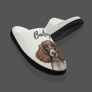 May include: White personalized slippers with a black sole and a brown and white dog illustration. The name "Bailey" is printed on the slipper.