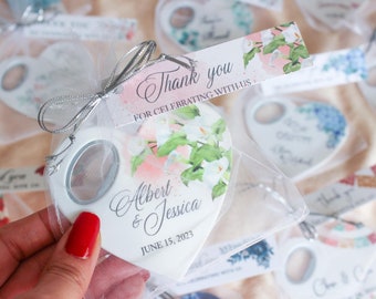May include: White heart-shaped bottle opener with a floral design and the text "Albert & Jessica June 15, 2023". The bottle opener is packaged in a white organza bag with a silver ribbon.