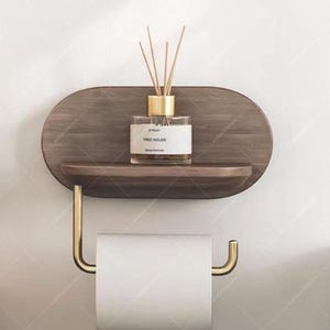 Puede incluir: Estante de baño de madera con un portarrollos dorado. El estante contiene una botella de vidrio con cañas y el texto "TREE HOUSE". El estante está montado en una pared blanca.