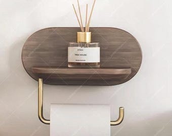 May include: A wooden bathroom shelf with a gold-colored toilet paper holder. The shelf holds a glass bottle with reeds and the text "TREE HOUSE". The shelf is mounted on a white wall.
