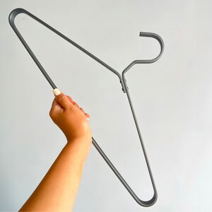 May include: A gray metal hanger with a hook at the top. The hanger is bent into a V-shape.