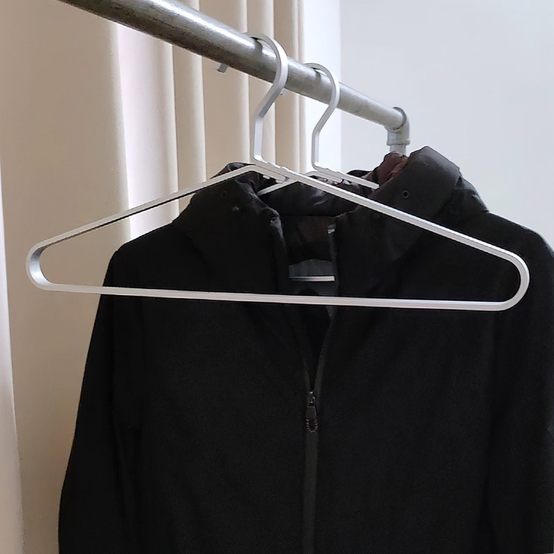 May include: A silver metal hanger with a black jacket hanging on it.
