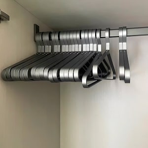 May include: A set of silver metal hangers hanging on a metal rod. The hangers are all the same size and shape, and they are arranged in a neat row.
