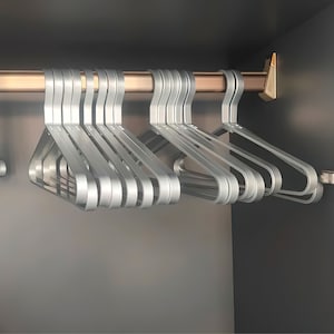 May include: A set of silver metal hangers hanging on a metal rod. The hangers are all the same size and shape, and they are arranged in a row.