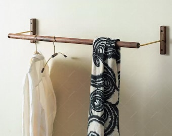 May include: A wooden wall-mounted clothing rack with brass accents. A white shirt hangs on a brass hanger to the left, and a black and white patterned scarf hangs on the right. The rack is mounted on a light-colored wall.