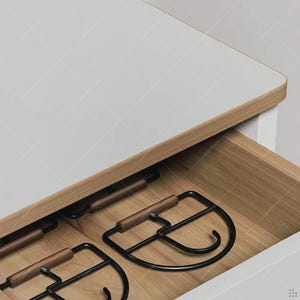 May include: A partially open wooden drawer with black metal and wood wine glass holders. The drawer is set into a white cabinet with a light wood trim.