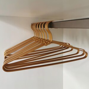 May include: A set of gold-colored plastic hangers. The hangers are stacked on top of each other and are hanging from a metal rod.