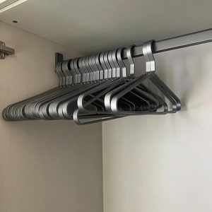 May include: A stack of silver metal hangers hanging on a metal rod in a closet.