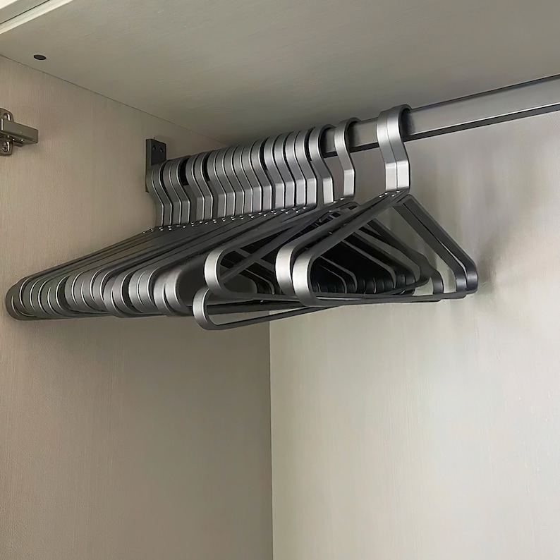 May include: A stack of silver metal hangers hanging on a metal rod in a closet.