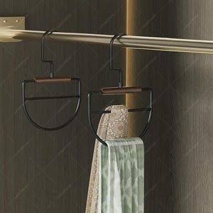 May include: Two black metal scarf hangers with wooden accents are suspended from a gold-colored rod. One hanger holds a patterned scarf, and the other is empty. The hangers have a semi-circular design.