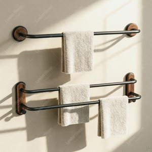 May include: Two wall-mounted towel racks featuring matte black metal bars and circular or rectangular wood-grain mounting plates. The top rack holds one beige towel, while the bottom double-bar rack holds two beige towels, creating a functional storage set.