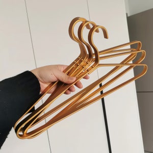 May include: Four gold metal hangers with a rounded shape and a textured surface. The hangers are stacked on top of each other.