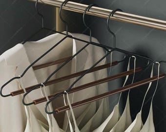May include: A collection of black metal clothes hangers with wooden bars, holding white camisoles and a white button-down shirt. The hangers are suspended from a gold-colored rod, creating a clean and organized display.