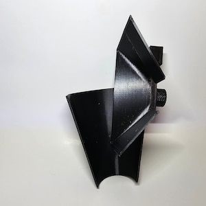 Puede incluir: Un objeto negro impreso en 3D con forma de embudo y una pequeña perilla redonda en el lateral.