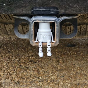 May include: A white plastic figure of a person with the text "10mm" printed on the body. The figure is attached to a black metal hitch receiver.