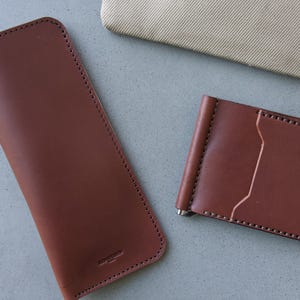 May include: Two brown leather wallets, one a long wallet and the other a money clip wallet.