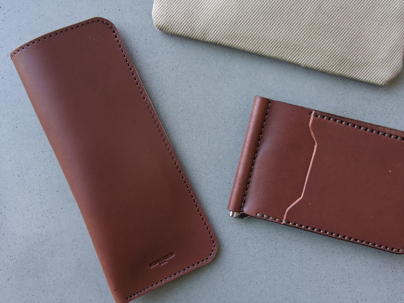 May include: Two brown leather wallets, one a long wallet and the other a money clip wallet.