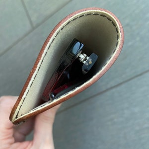 May include: A brown leather glasses case with a white lining. The case is open and a pair of glasses is inside.