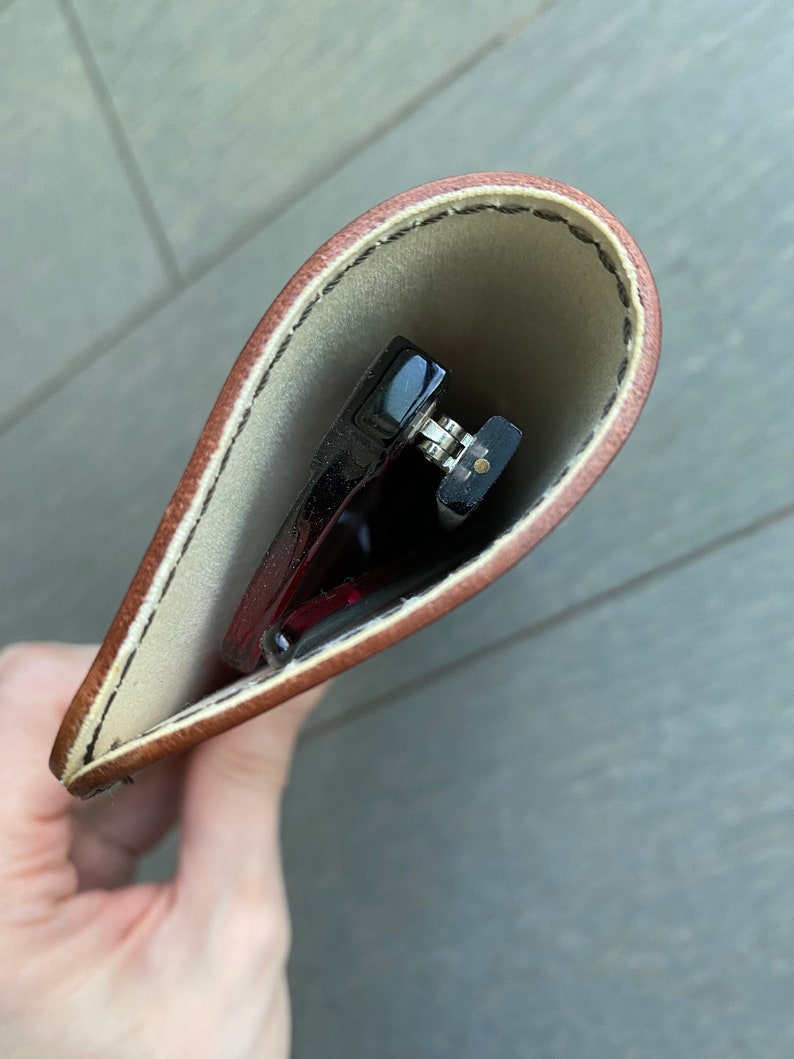 May include: A brown leather glasses case with a white lining. The case is open and a pair of glasses is inside.