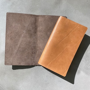 May include: A brown leather notebook with a brown suede cover. The notebook is open and the cover is folded back.