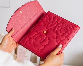 Op de afbeelding: Een roze quilted clutch met een bloemenpatroon. De clutch heeft een gouden knoopsluiting en is open om een roze interieur te onthullen.