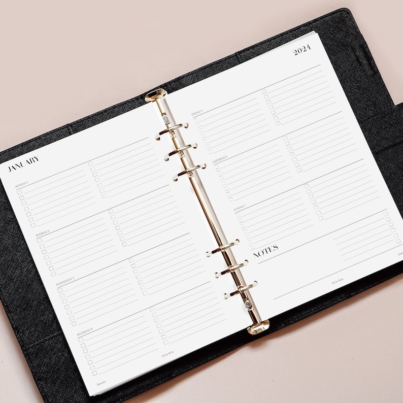 May include: A black planner with a gold ring binder. The planner is open to January 2024 and has a weekly layout with space for notes.