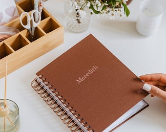 May include: A brown spiral bound journal with the name Meredith printed in pink on the front cover.