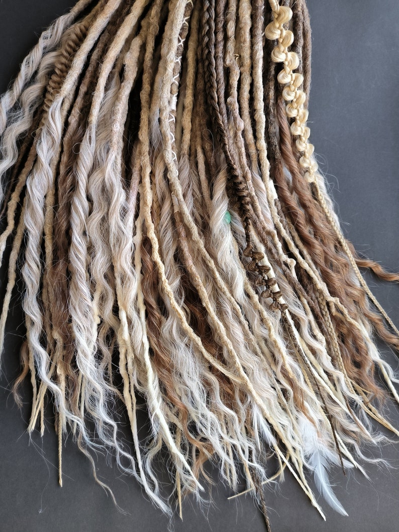 May include: A set of brown and white synthetic dreadlocks. The dreadlocks are made of a variety of textures, including straight, wavy, and curly. The dreadlocks are tied together at the top with a brown string.