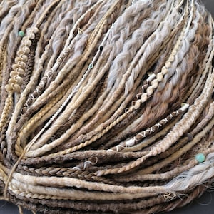 May include: A bundle of synthetic dreadlocks in shades of brown, blonde, and white. The dreadlocks are tied together with a string and have beads and other decorative elements.