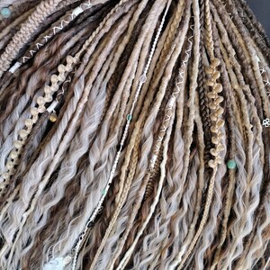 May include: A set of synthetic dreadlocks in various shades of brown, beige, and white. The dreadlocks are decorated with beads and feathers.