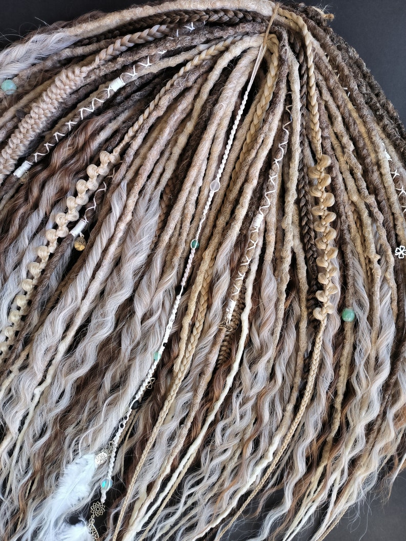 May include: A set of synthetic dreadlocks in various shades of brown, beige, and white. The dreadlocks are decorated with beads and feathers.