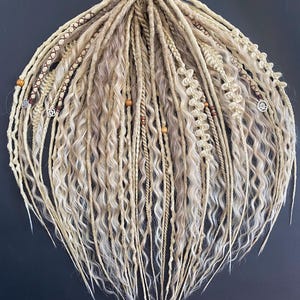 Può includere: Un set di dreadlock sintetiche bionde e castano chiaro con perline e ciondoli. Le dreadlock sono ondulate e hanno un aspetto naturale.