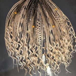 Può includere: Dreadlocks fatti a mano nei toni del biondo, marrone e grigio, con estremità ricce. I dread sono adornati con perline decorative, ciondoli e piume. Extension per capelli acconciate in modo unico e artistico.