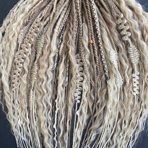 Könnte beinhalten: Ein Set aus blonden und braunen synthetischen Dreadlocks mit verschiedenen Texturen und Verzierungen, darunter Perlen und Charms.