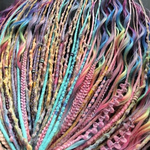 Puede incluir: Una colección de rastas multicolores en tonos pastel de rosa, azul, amarillo y morado. Las rastas están adornadas con cuentas y otros adornos. La imagen muestra una variedad de texturas y estilos, creando una exhibición vibrante y artística.