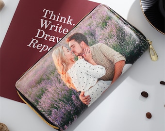 Puede incluir: Una cartera con cremallera con una foto de una pareja besándose en un campo de flores moradas. La foto está impresa en la parte delantera de la cartera.