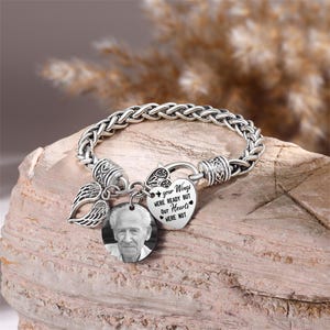 Puede incluir: Pulsera de plata con un dije en forma de coraz&oacute;n que dice "Tus alas estaban listas pero nuestros corazones no". El dije est&aacute; unido a un dije de ala de &aacute;ngel de plata y a un dije de foto redondo con una foto en blanco y negro de un hombre mayor.