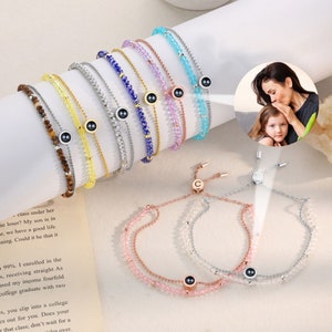May include: A set of colorful beaded bracelets with a hidden photo charm. Each bracelet features a different color of beads and a small, round charm with a hidden photo inside. The charms are silver with a black center. The bracelets are adjustable with a sliding knot.