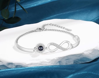 May include: Silver infinity bracelet with a small black pearl in a circle setting. The bracelet has a chain link closure.