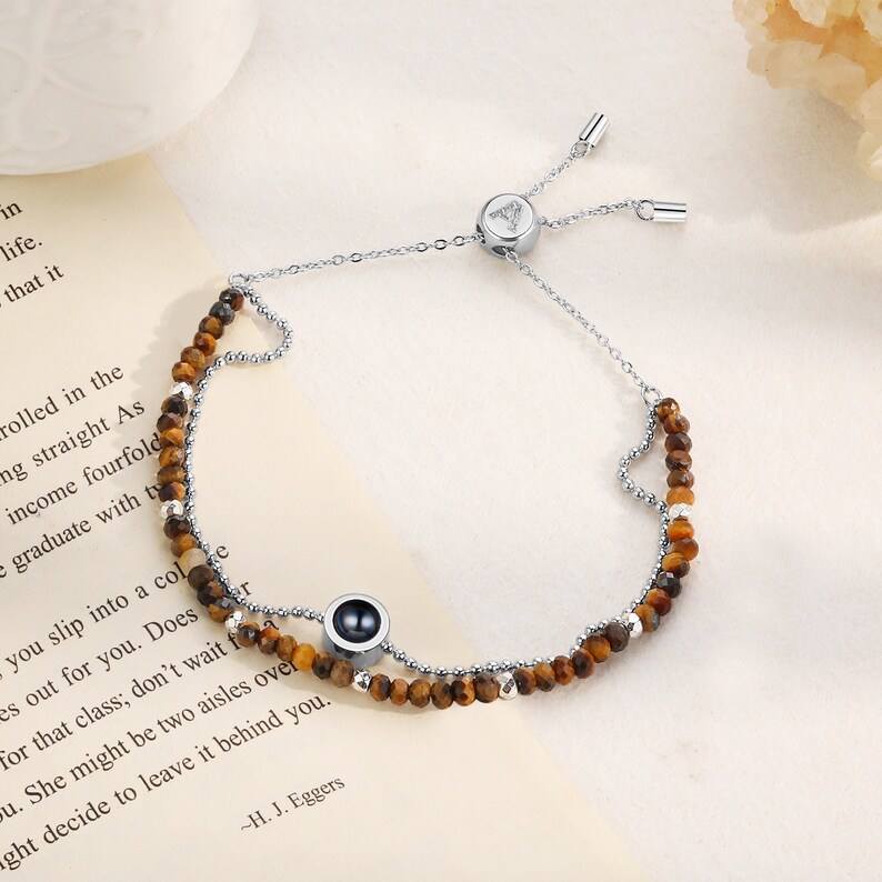 May include: A silver chain bracelet with a tiger's eye bead and a black stone charm. The bracelet has a sliding clasp for adjustable sizing.