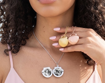 May include: A silver-toned shell-shaped locket necklace featuring two circular black and white photographs inside. The locket hangs on a delicate chain. Two additional shell-shaped pendants in gold and rose gold tones are held in the hand.