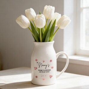 Op de afbeelding: Een witte keramische vaas met een handvat, gevuld met witte tulpen. De vaas heeft de tekst "If Nanny's were flowers I'd pick you!" en roze bloemaccenten. Een attent cadeau.