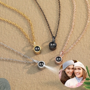 May include: Four necklaces with different colored chains and pendants. The pendants are small, round, and have a black center. The necklaces are displayed on a brown surface.