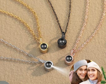 May include: Four necklaces with different colored chains and pendants. The pendants are small, round, and have a black center. The necklaces are displayed on a brown surface.