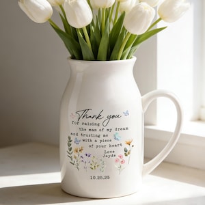 Puede incluir: Una jarra de cerámica blanca con asa, llena de tulipanes blancos. La jarra tiene un diseño floral y el texto "Thank you" con un mensaje personalizado y fecha. Un regalo atento para cualquier ocasión.