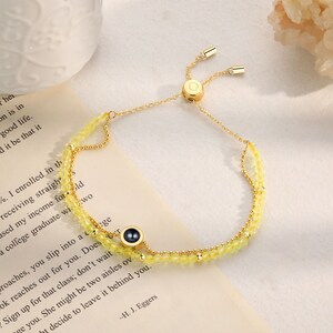 May include: A gold chain bracelet with a yellow crystal bead design. The bracelet has a sliding clasp and a small black circle charm with a gold rim.
